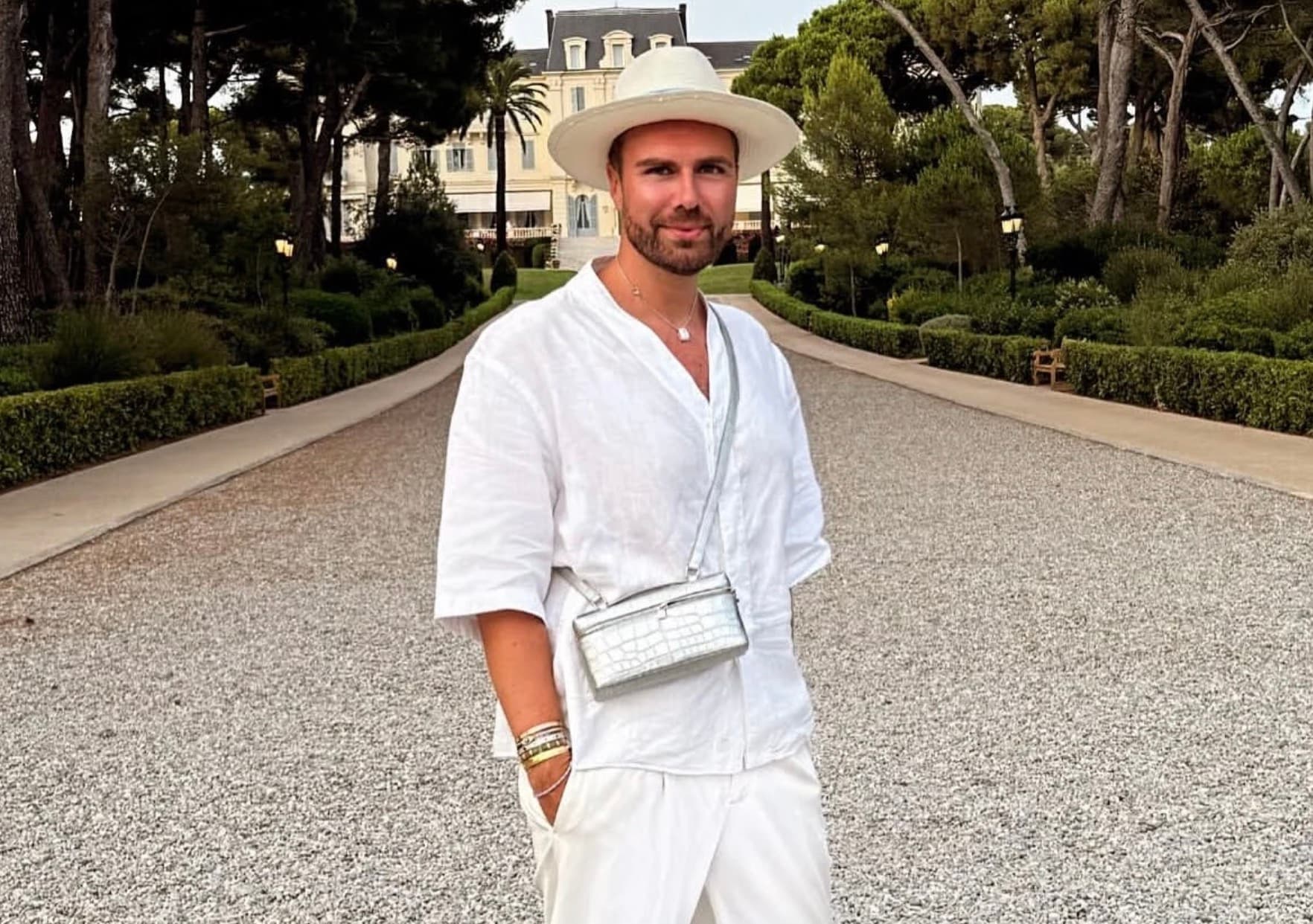 André Borchers in a white linen outfit and wide-brimmed hat on a garden path with a chateau behind him