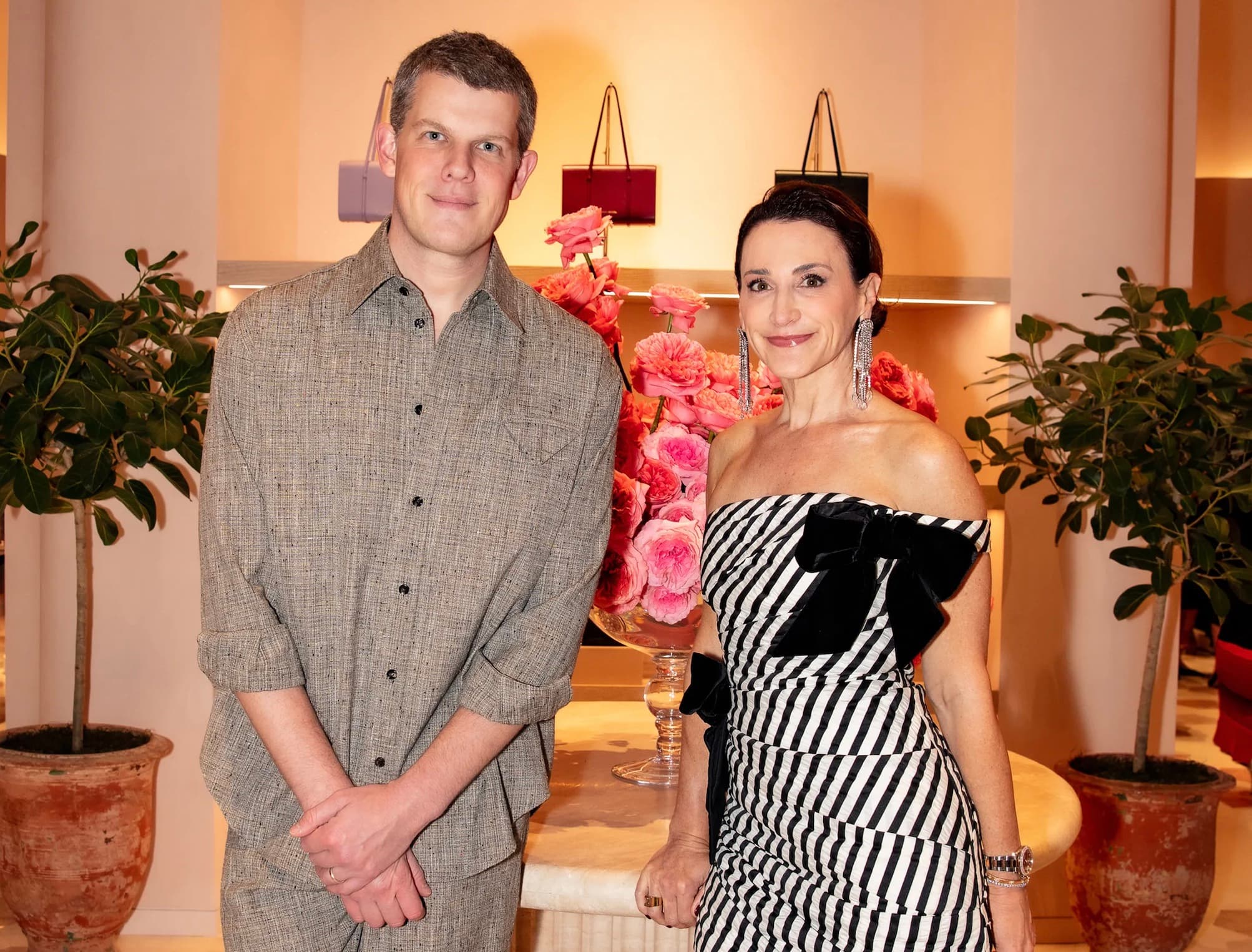Wes Gordon and Carolina Herrera posing together in a boutique surrounded by pink roses