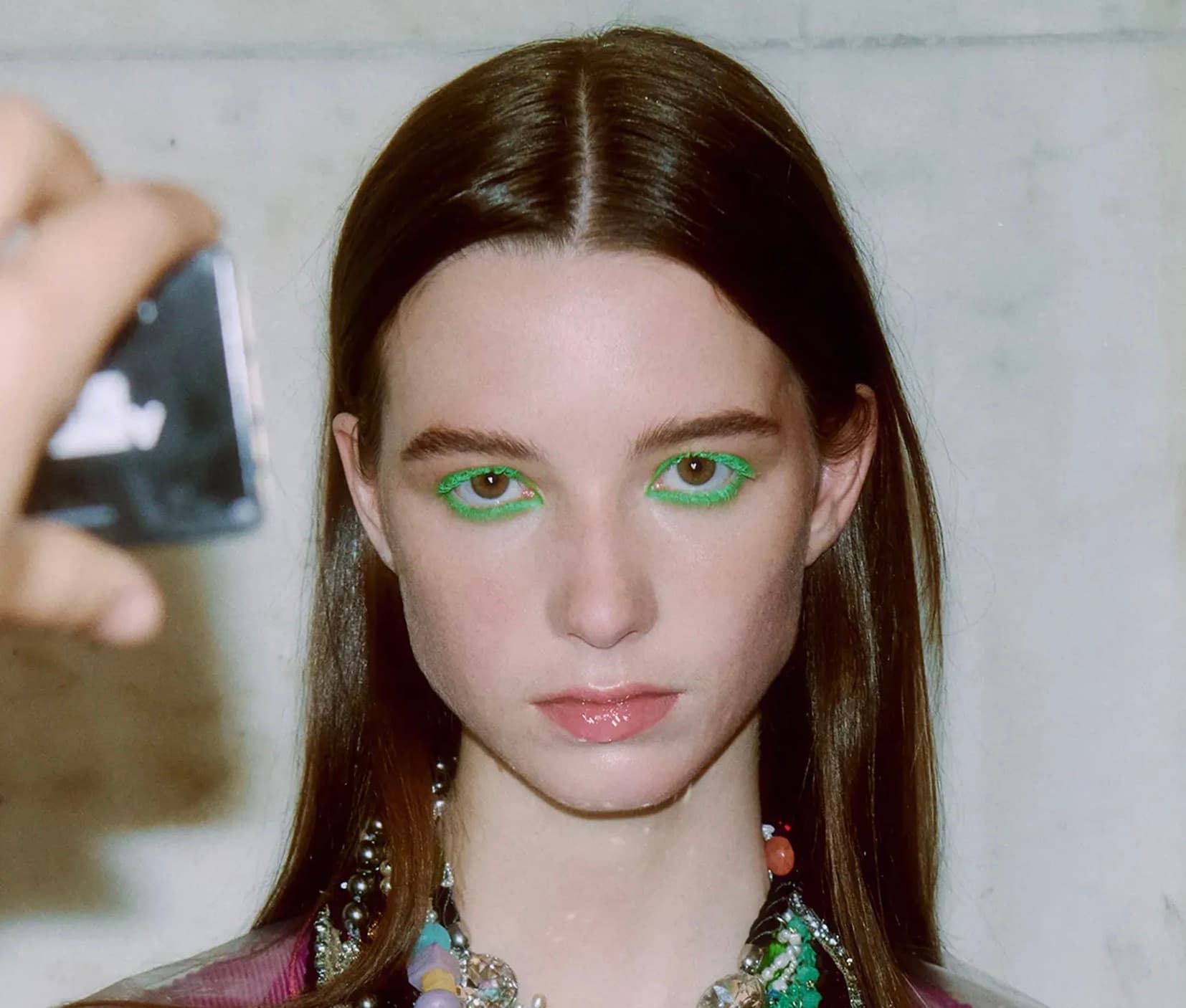 Model with bold green graphic eyeliner backstage at a fashion show
