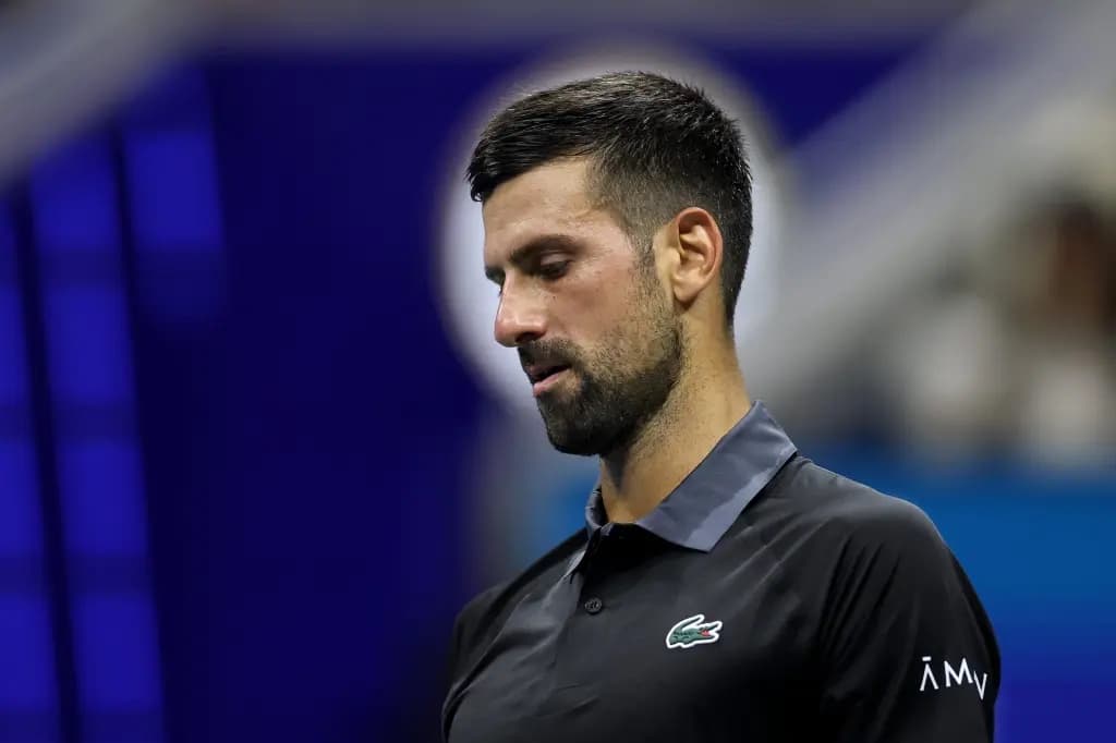 Novak Djokovic looking down with a dejected expression in a dark polo shirt