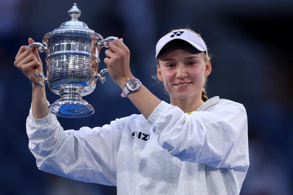 Elena Rybakina smiling and holding up the US Open championship trophy