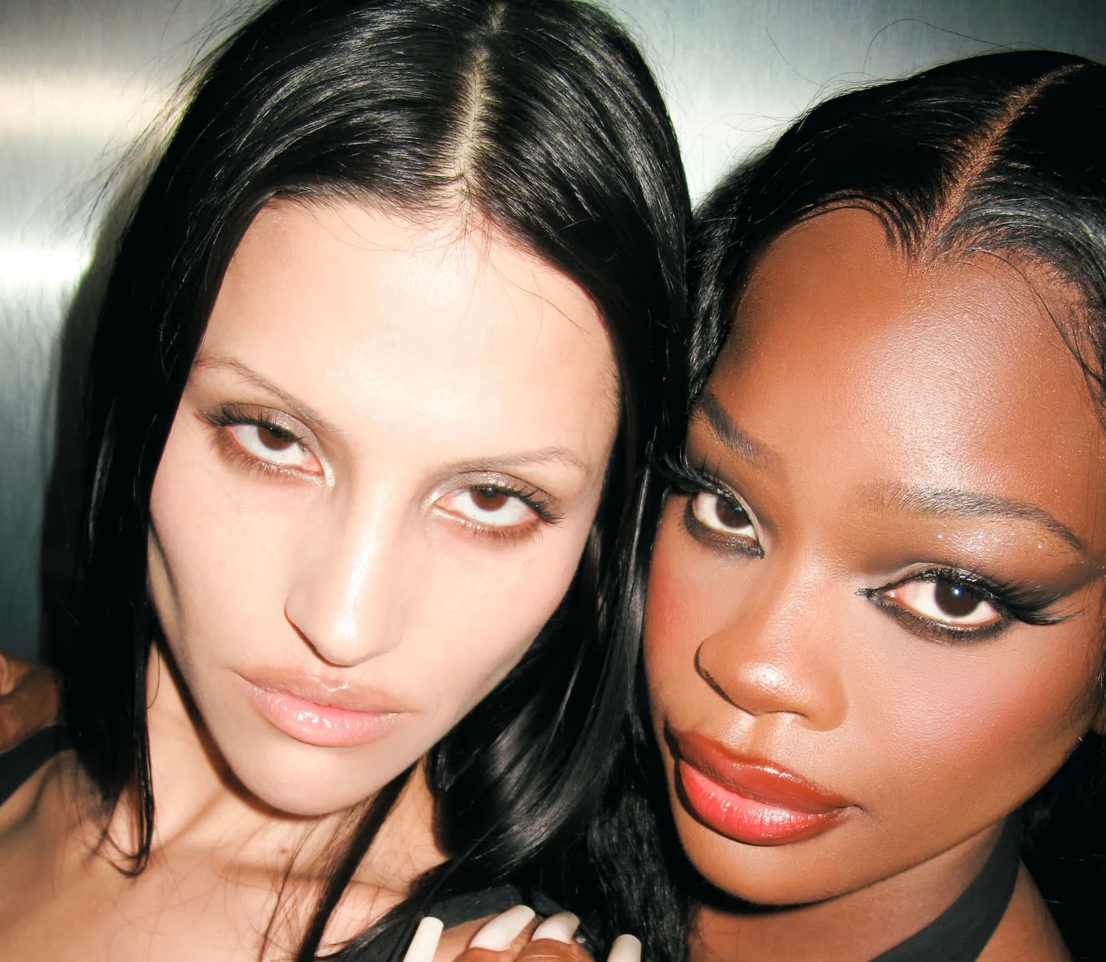 Two models with dramatic makeup looks pressed close together for a beauty campaign