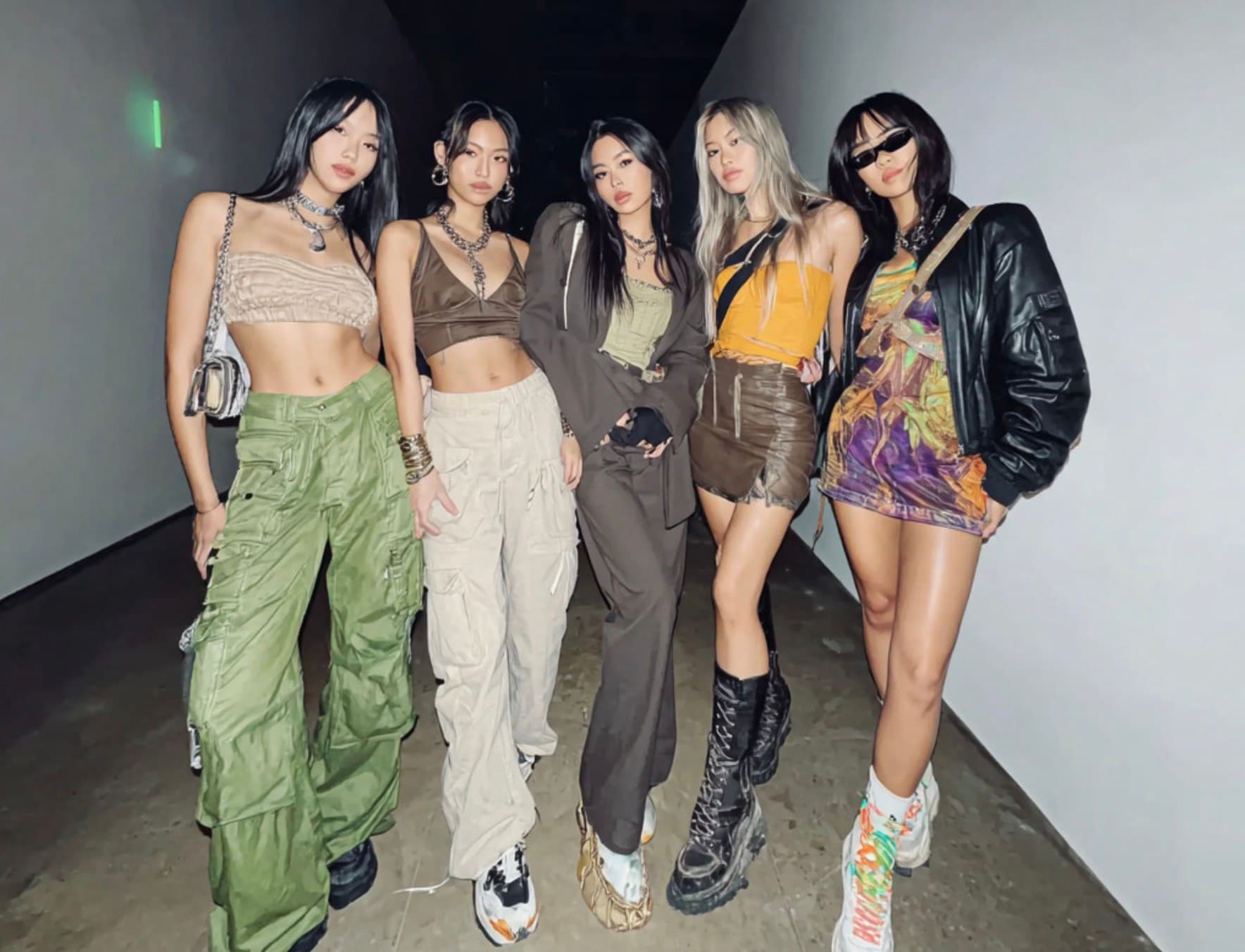 A girl group posing together in coordinated streetwear, cargo pants, crop tops and chunky boots