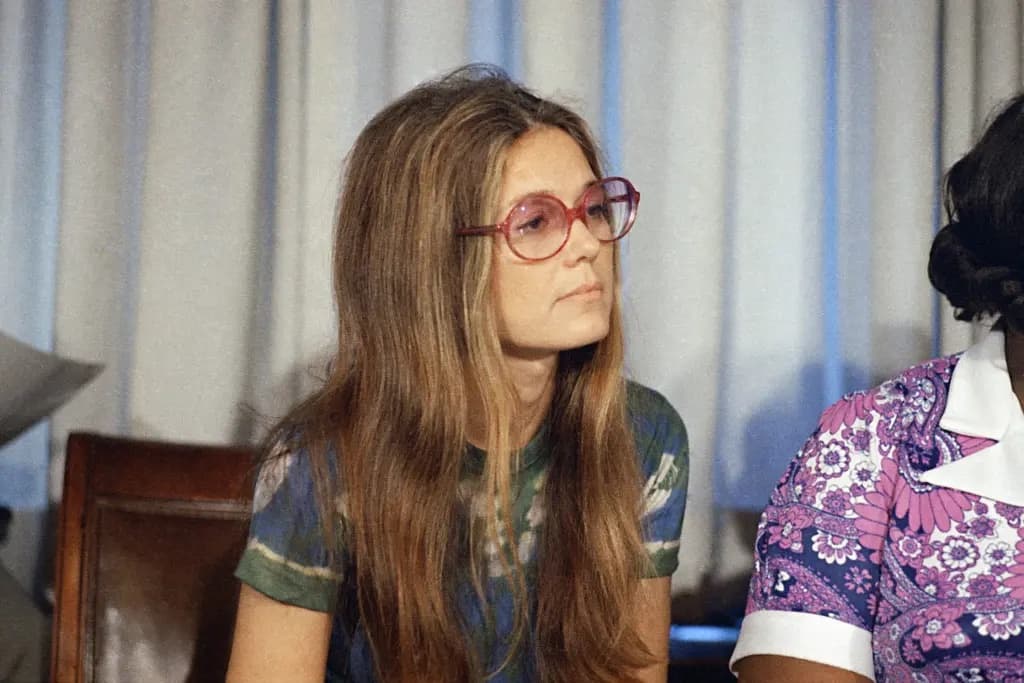 Gloria Steinem wearing red glasses at a press event in the 1970s