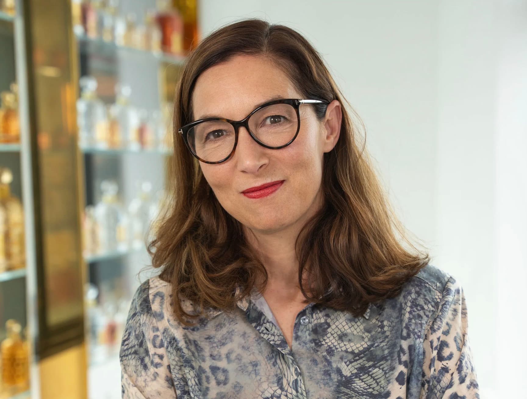 Delphine Jelk, Guerlain's perfumer, smiling in front of a shelf of perfume bottles
