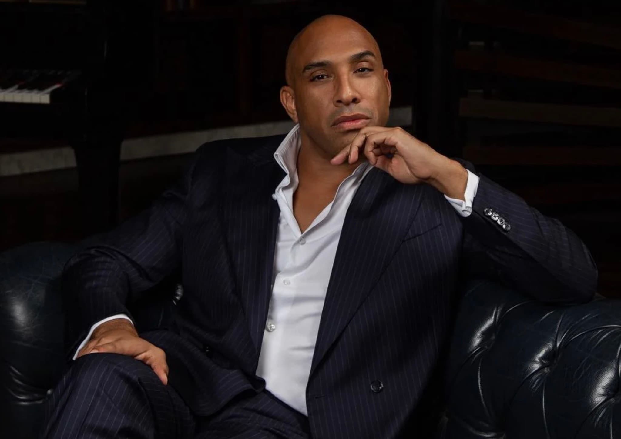 Maurice Momo Mobetie in a navy pinstripe suit seated in a leather armchair