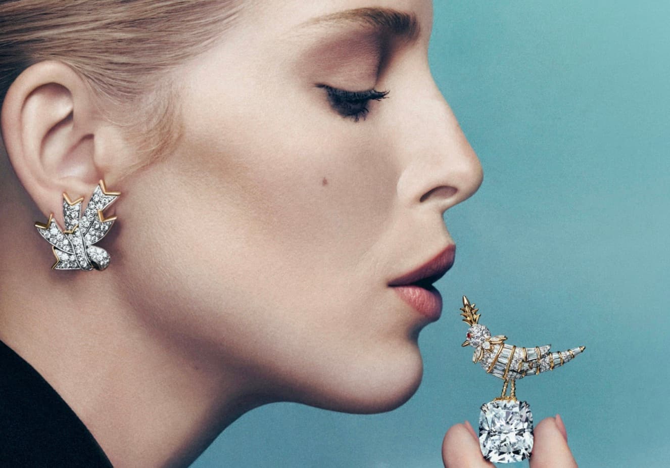 Model in profile wearing a diamond leaf earring beside a Tiffany Bird on a Rock brooch perched on a large cushion cut diamond