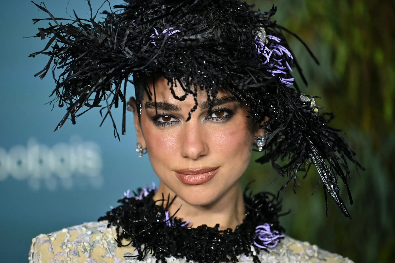 Dua Lipa wearing an oversized black feathered Chanel couture hat with lavender accents
