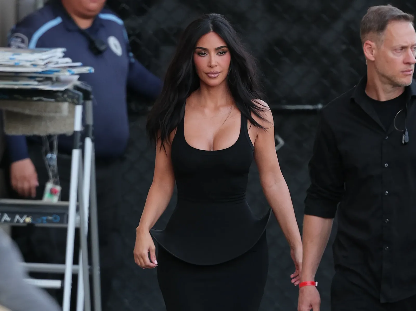 Kim Kardashian walking in a black scoop neck peplum dress