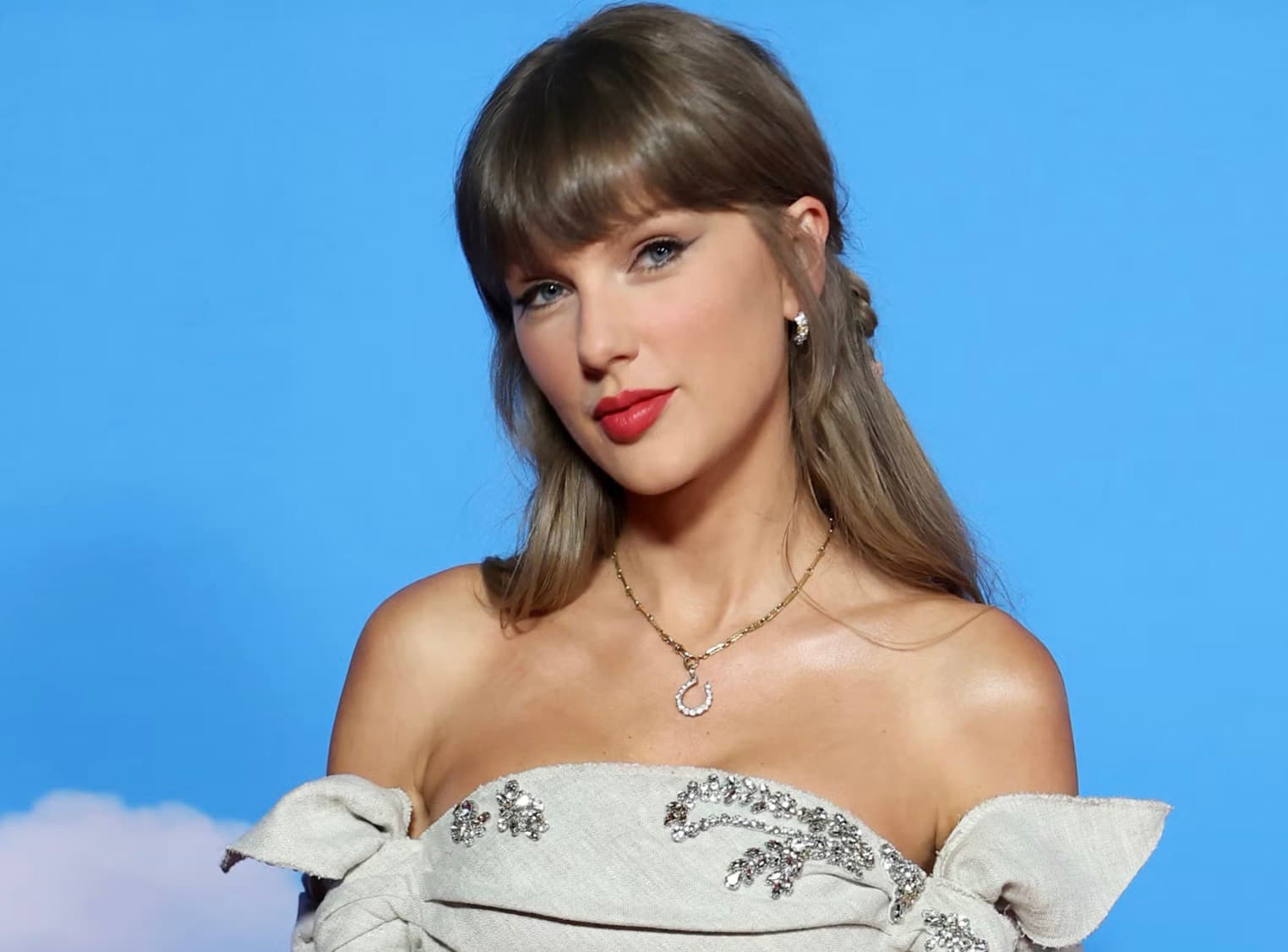 Taylor Swift in a strapless crystal embellished gown against a blue backdrop