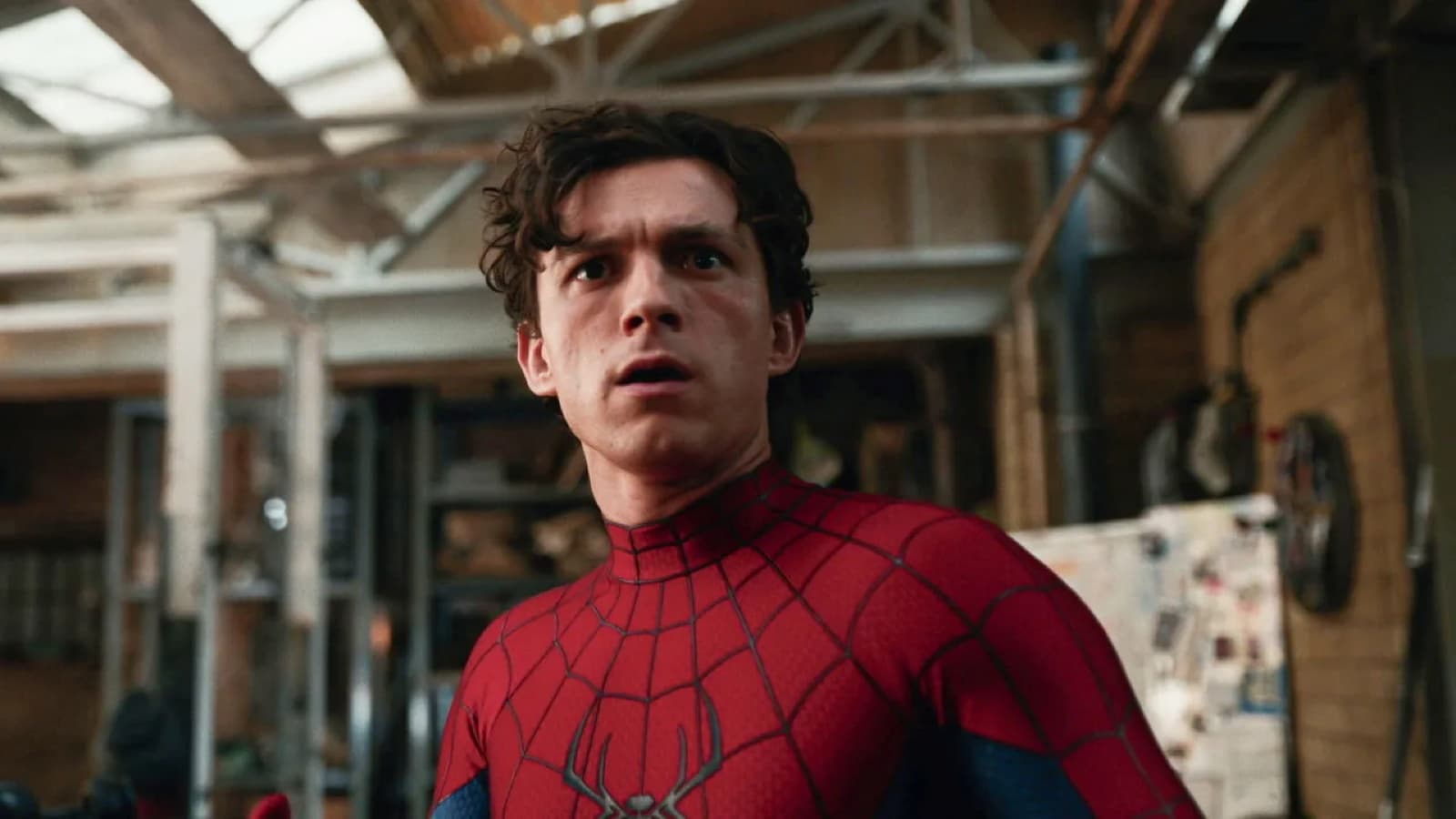 Tom Holland in the Spider-Man suit, looking off camera inside a workshop